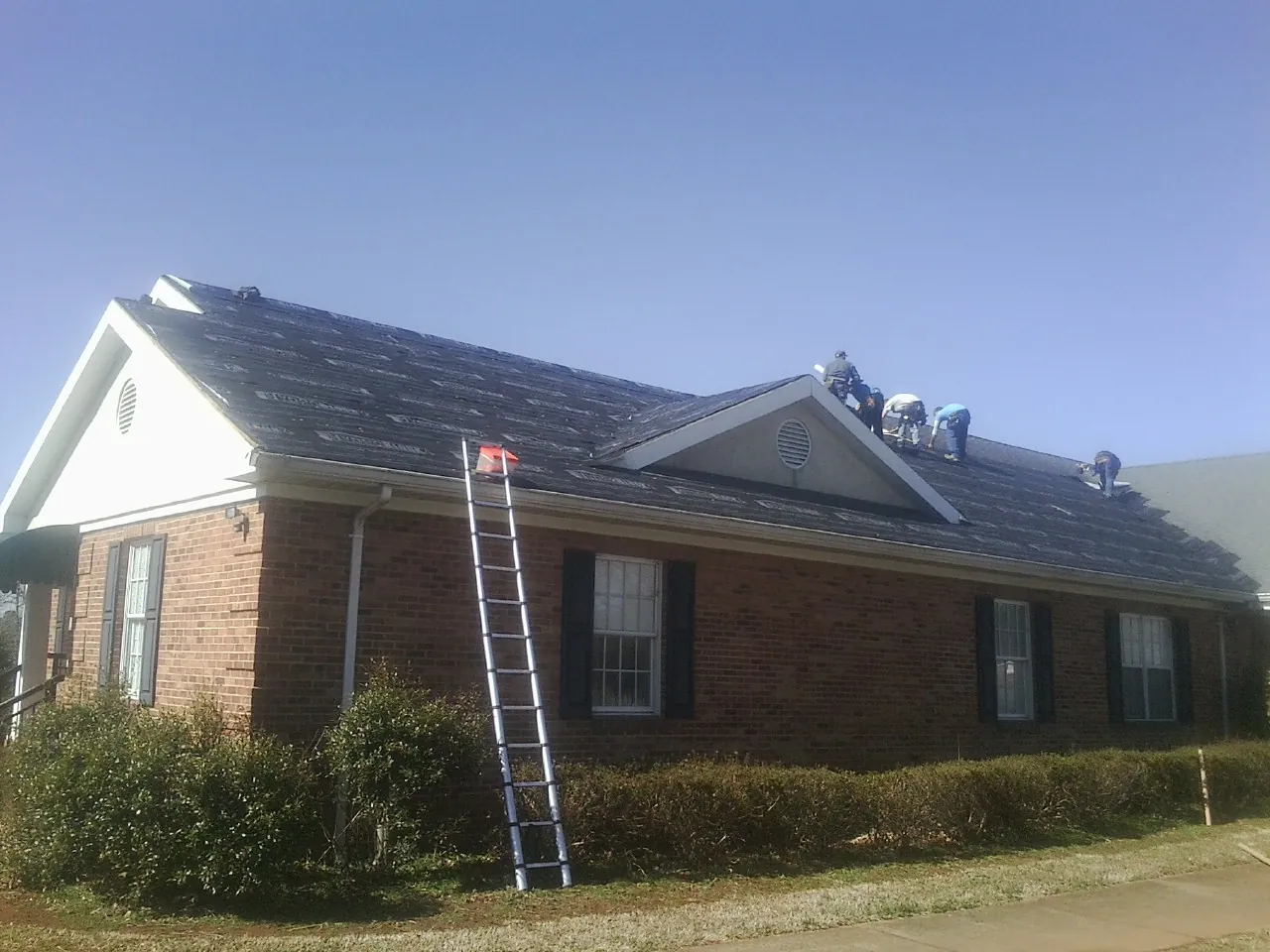 Crew tearing shingles off a brick ranch roof with a ladder set — Metal Roof Repair work by our crew in Fogelsville