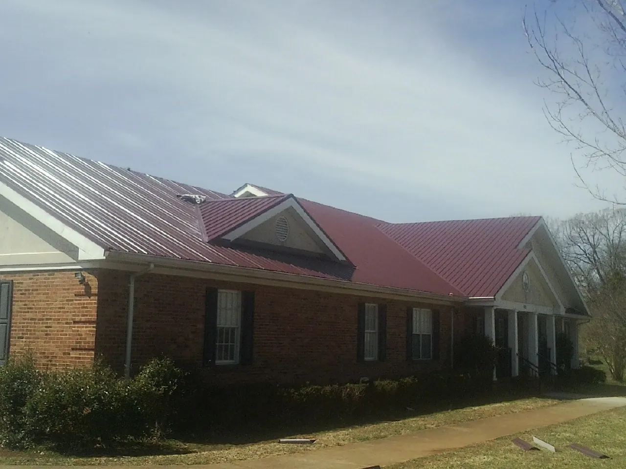 Red metal roof with gabled entries on a long brick building, from a Hail Damage Roof Repair job in Fogelsville