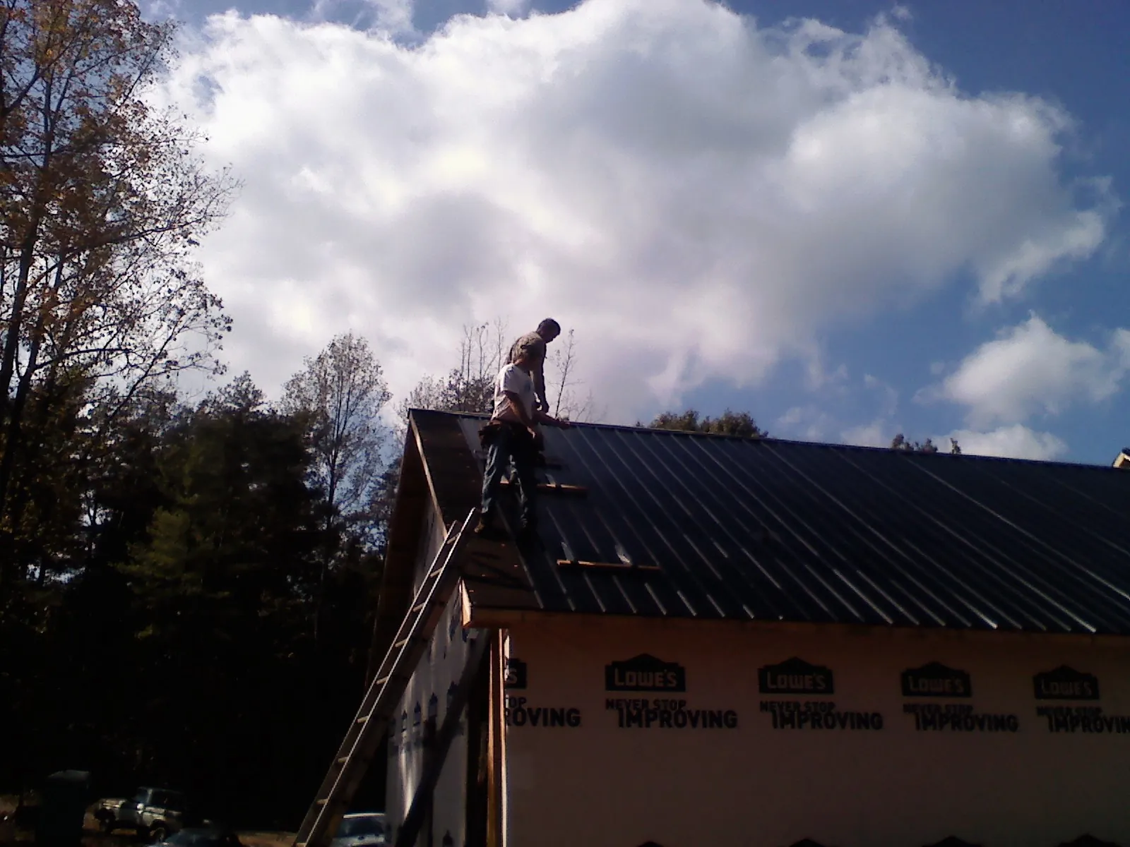 Roofer fastening dark metal panels high against a cloudy sky, from a Roof Inspection job in Fogelsville