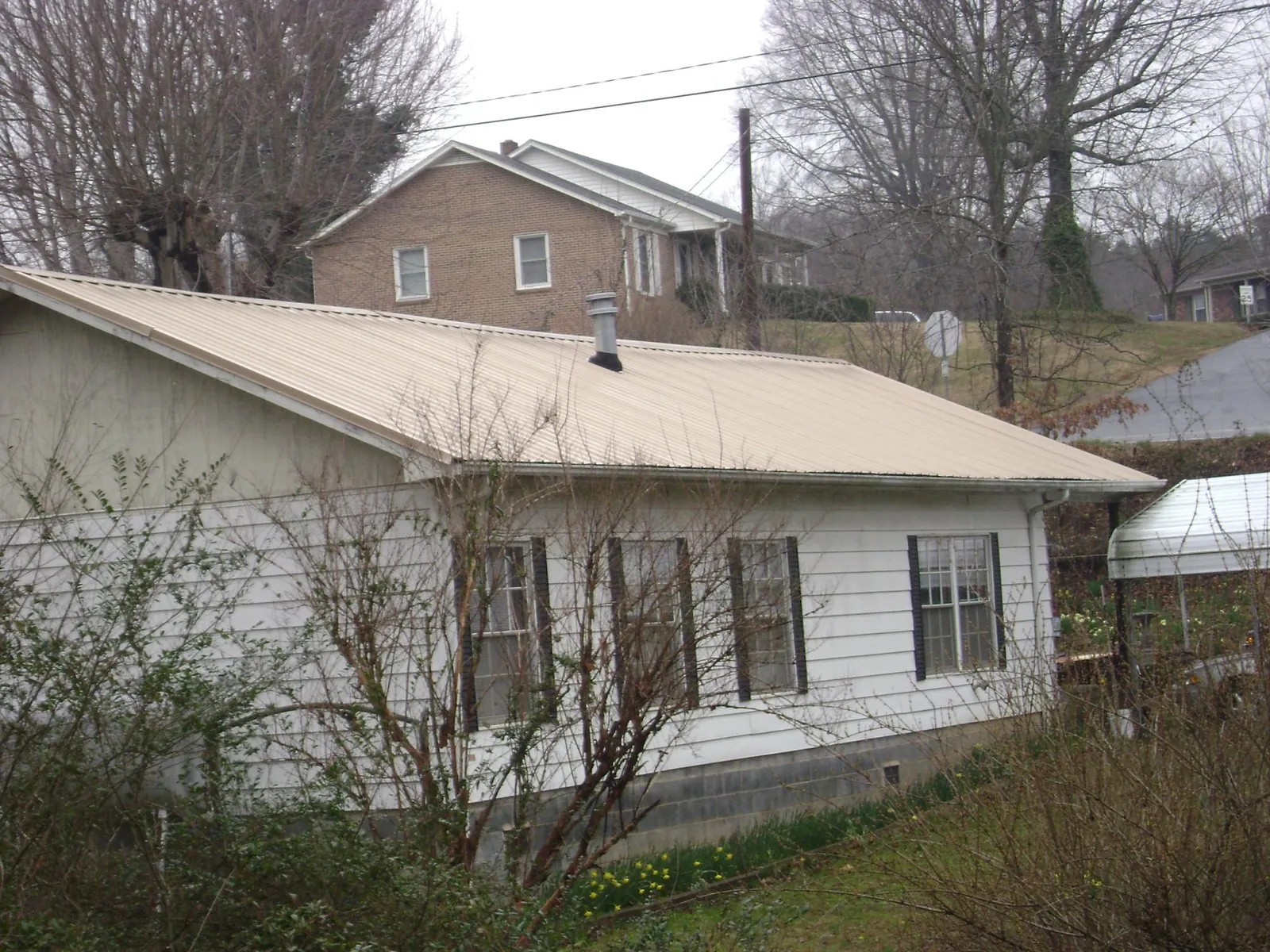 Tan metal roof on a white sided house set into a hillside — Commercial Roofing by Roofing Brothers in Fogelsville
